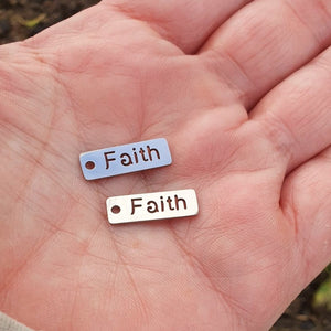 Berlock med text "Faith" i rostfritt stål